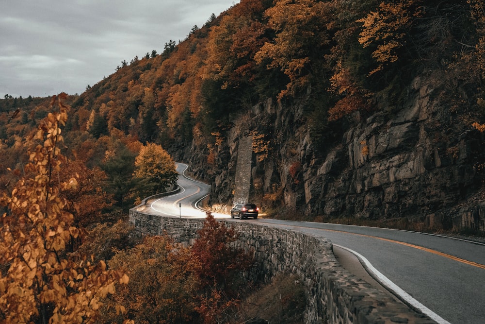 a road with a car on it and a cliff with trees on it