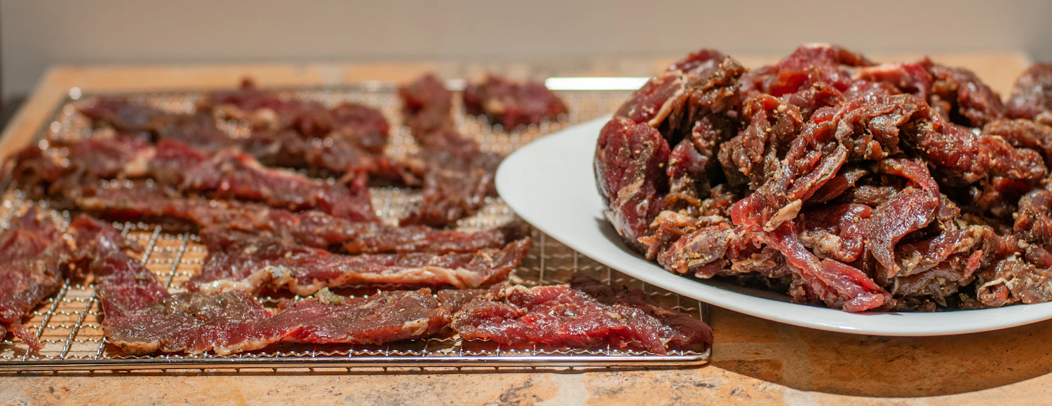 Red chile-marinated beef strips laid out on drying racks beside a full plate of finished jerky