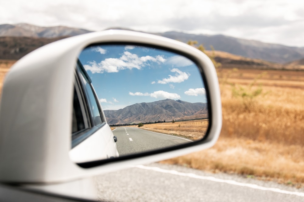 a side view mirror showing a car driving on a road