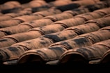 Rows of terracotta roof tiles are neatly aligned, with visible signs of weathering and aging. The tiles have a natural reddish-brown color with patches of dark discoloration, possibly due to moss or dirt.