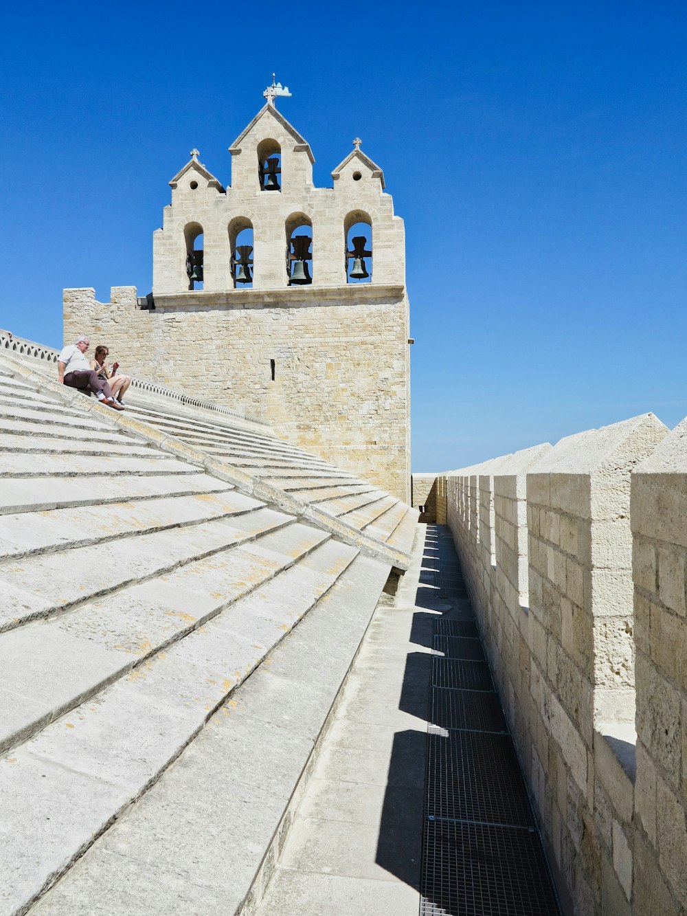 a stone building with a tower and a couple people sitting on the steps