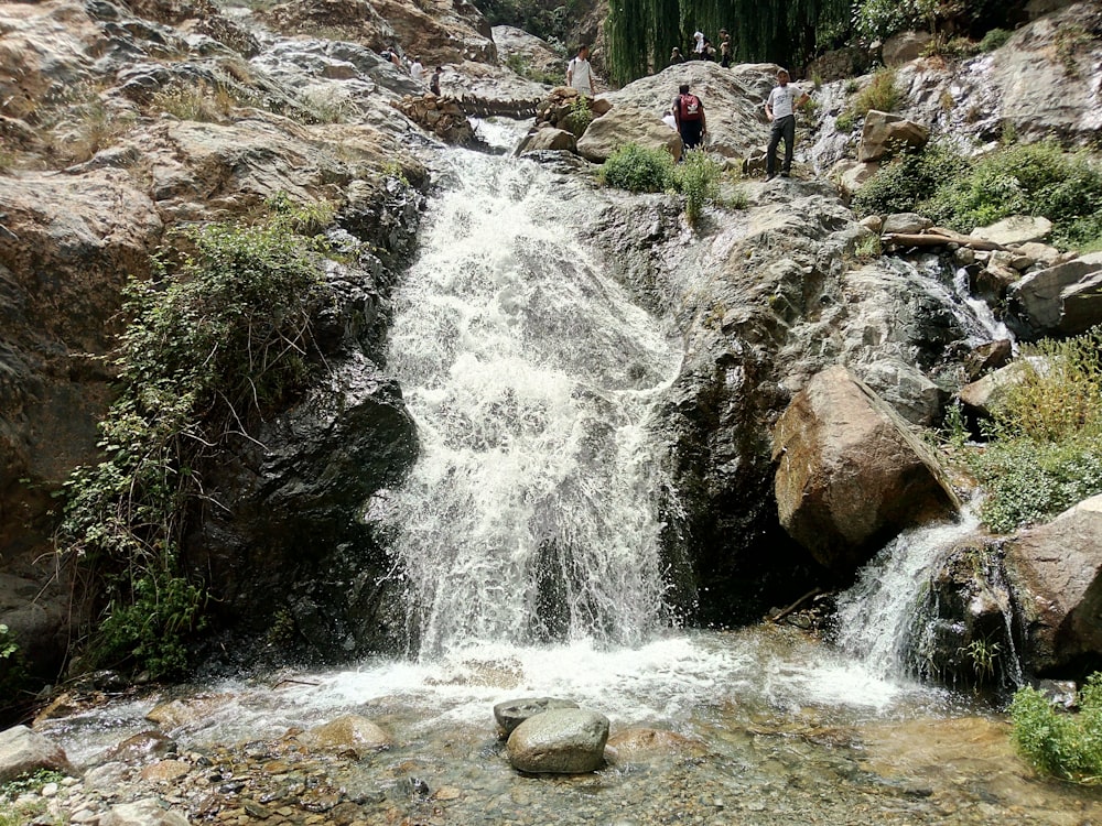 people standing on a rocky hillside next to a waterfall