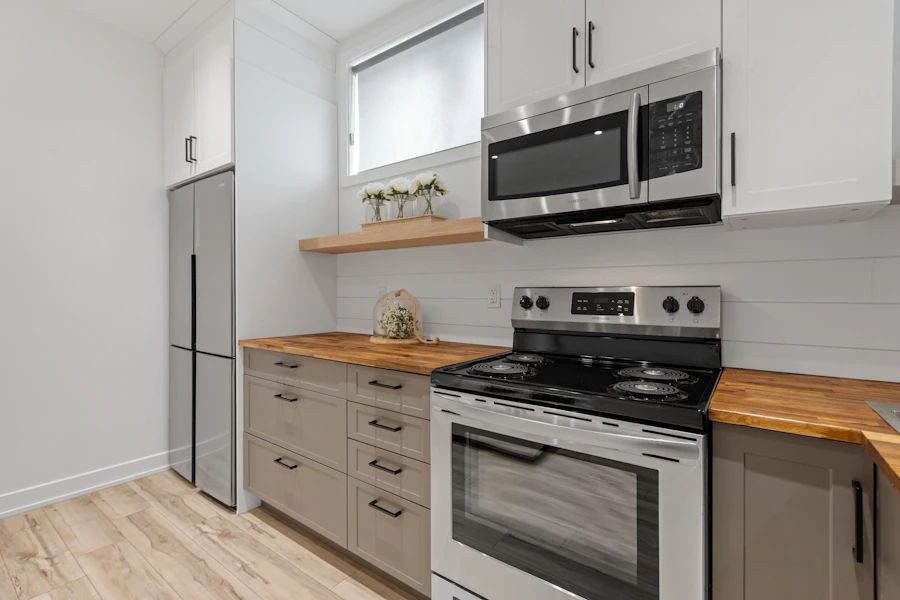 Close-up of white kitchen cabinets with stainless steel appliances and a wood countertop.