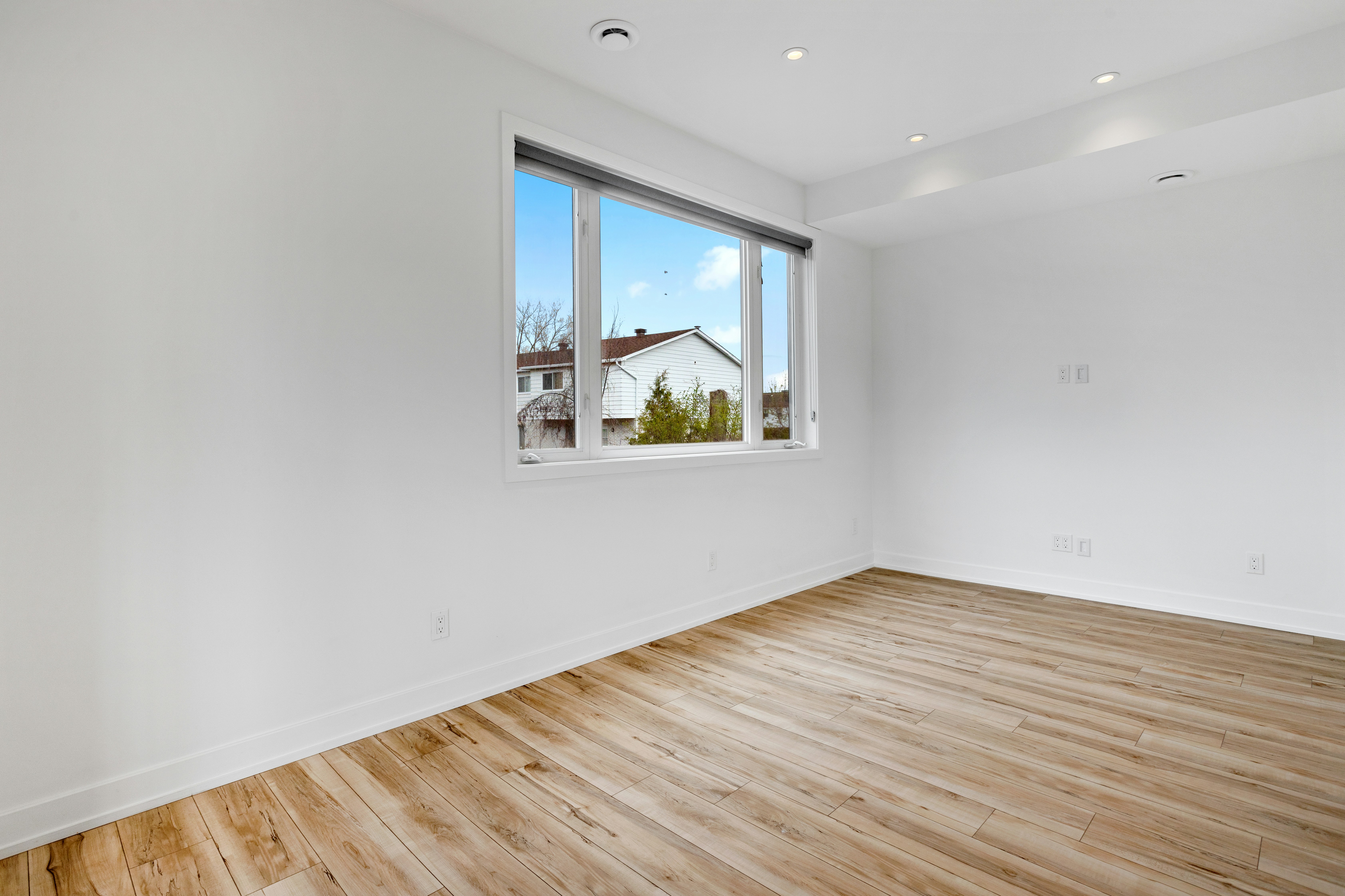 a room with a wood floor and a window with a view of a house and trees