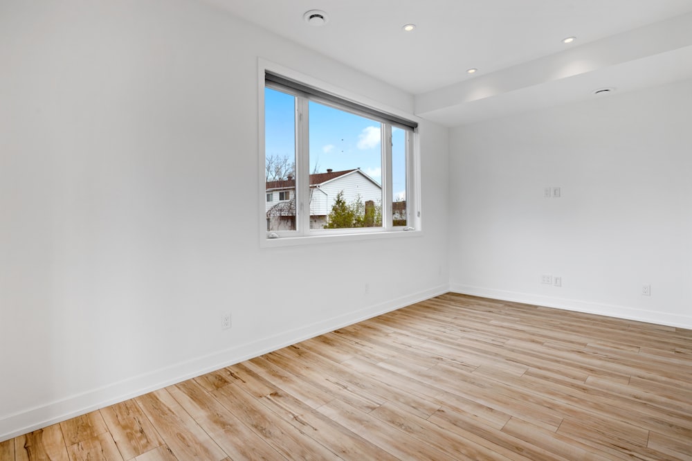a room with a wood floor and a window with a view of a house and trees