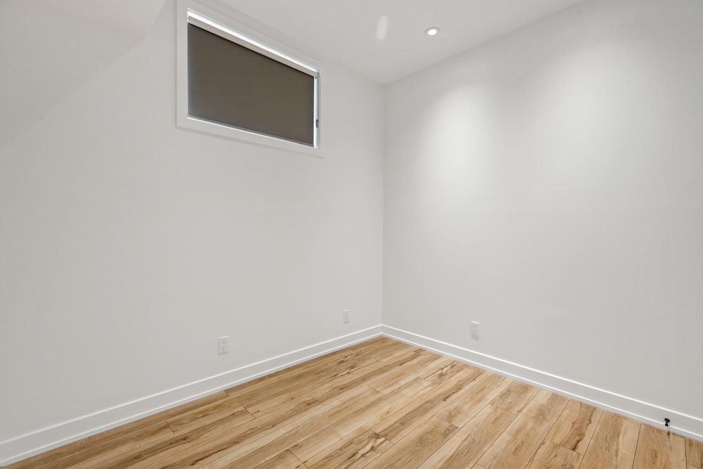 a room with a wood floor and a white wall with a window