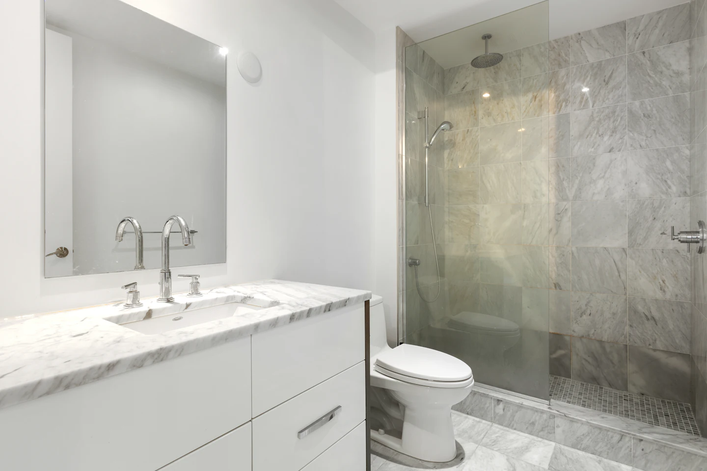 White vanity and a glass shower with gray stone-look tile