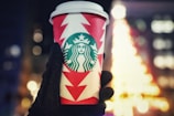 A hand holding a personalized cup with a festive design.
