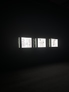 Three illuminated screens are set against a dark background, each displaying hand-drawn illustrations of various objects or scenes. The images on the screens appear to be simplistic line drawings, possibly resembling abstract art or sketches.