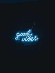 Neon blue letters spelling 'good vibes' illuminate against a dark background, giving off a cool and serene atmosphere.