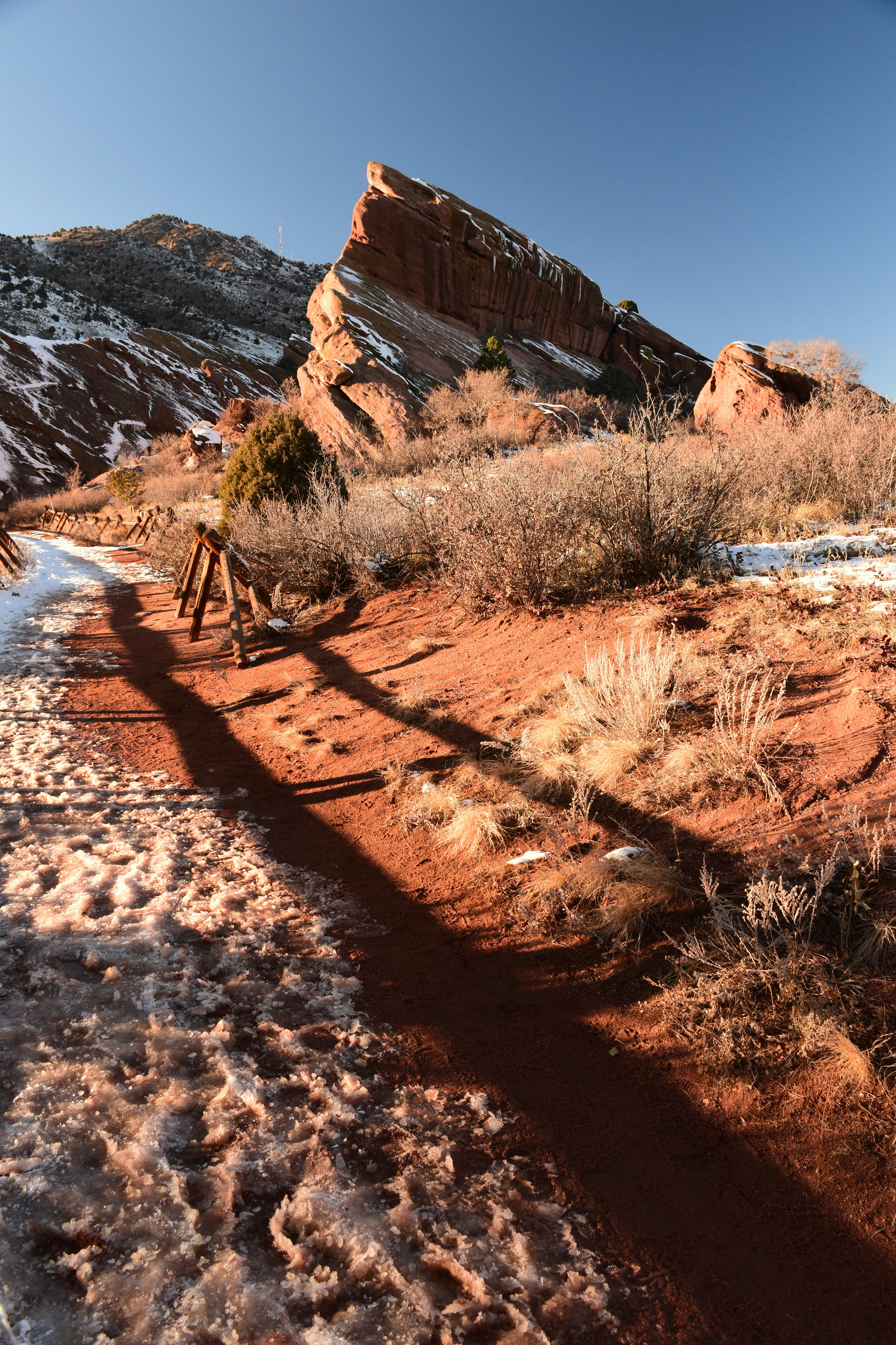 a dirt road with a bridge over it and a rocky hill in the background