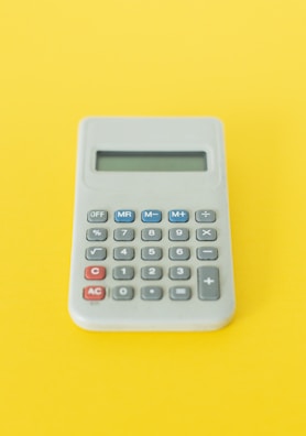 A compact silver calculator with a bright LCD screen beside a notebook.