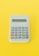 A simple electronic calculator with a gray body and standard number and function keys. It is set against a bright yellow background, highlighting the calculator as the central focus of the image.