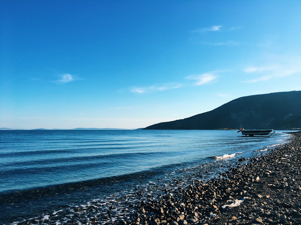 a rocky beach with a boat in the water and a hill in the background