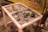 A small, weathered table holds several burnt offerings, including incense sticks and charred bowls. A burnt matchbox and remnants of ash are scattered across the dusty surface. In the background, there is a yellow metal panel with Hindi script.
