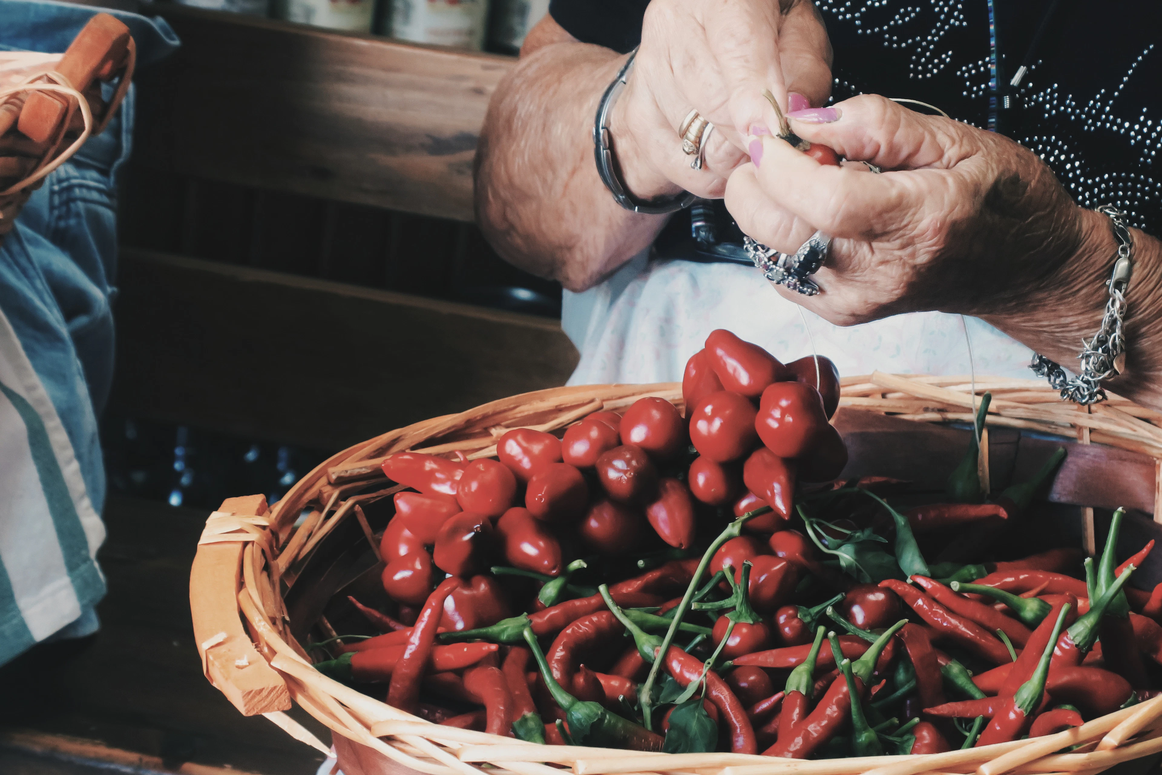 Weathered hands sorting fresh red chillies in a wicker basket, ready to be strung into the long drying braids of Italian tradition