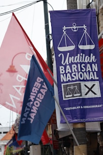Colorful political banners and flags are displayed in an outdoor setting, featuring campaign slogans and symbols.