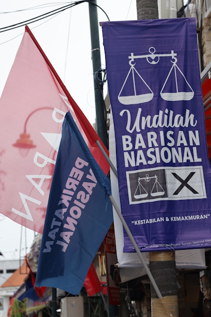 Colorful political banners and flags are displayed in an outdoor setting, featuring campaign slogans and symbols.