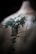 An abstract, detailed tattoo is depicted on a person's back, featuring intricate designs and text in a vertical alignment. The tattoo has a dark green to black color scheme, with sharp, defined lines and some blurred areas, creating a mysterious and artistic effect.