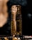 A decorative perfume bottle with intricate gold and brown patterns, placed against a dark background. Surrounding the bottle are beads and smoke, adding a luxurious and mysterious atmosphere.