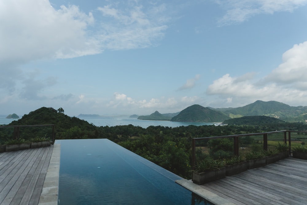 a pool with a deck and trees by it and mountains in the background