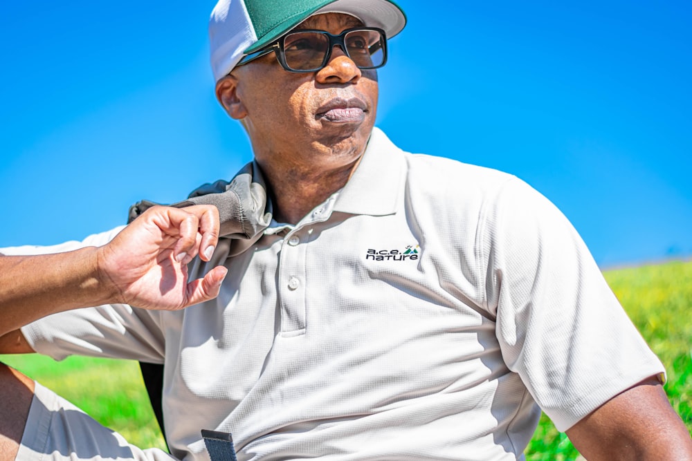 a man wearing a hat and glasses sitting in a field