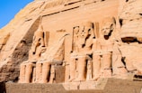 a stone wall with carvings with Abu Simbel temples in the background