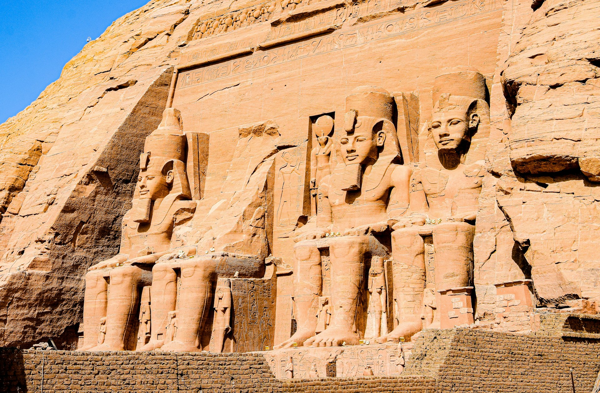 a stone wall with carvings with Abu Simbel temples in the background