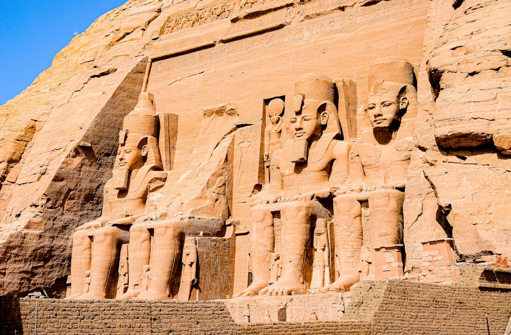 un mur de pierre avec des sculptures avec les temples d’Abou Simbel en arrière-plan