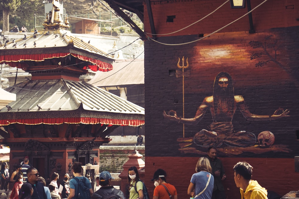 a group of people walking around a building with a large painting on it