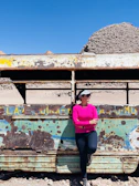 A woman wearing a hot pink western shirt with modern black font designs, standing against a desert backdrop.