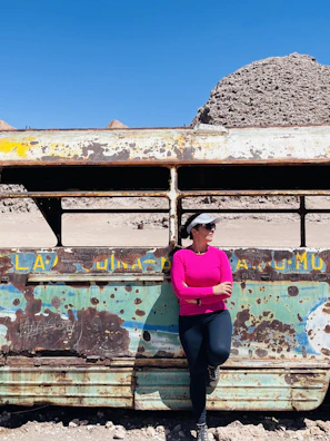 A woman wearing a hot pink western shirt with modern black font designs, standing against a desert backdrop.