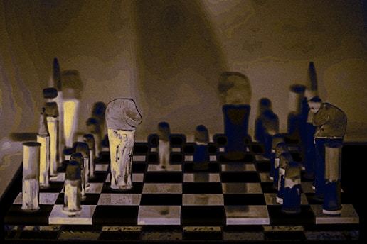 A stylized image of a chessboard with vertically elongated, abstract chess pieces. The pieces have an artistic, distorted appearance with a mix of dark and light tones that create a surreal atmosphere. The background is muted, focusing attention on the chessboard and its unique pieces.