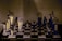 A stylized image of a chessboard with vertically elongated, abstract chess pieces. The pieces have an artistic, distorted appearance with a mix of dark and light tones that create a surreal atmosphere. The background is muted, focusing attention on the chessboard and its unique pieces.
