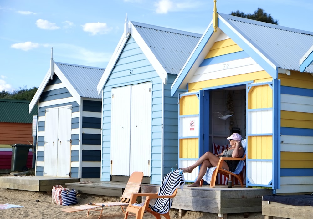 a person sitting on a chair outside a small yellow and blue building