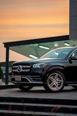 A sleek black Mercedes parked in front of a modern office building at sunset.