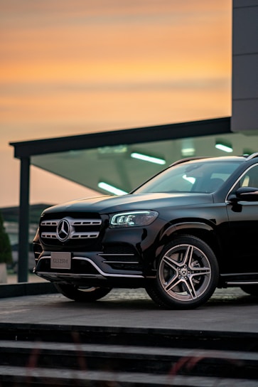 Luxy Limousine sleek black Mercedes parked in front of Geneva airport terminal during sunset.