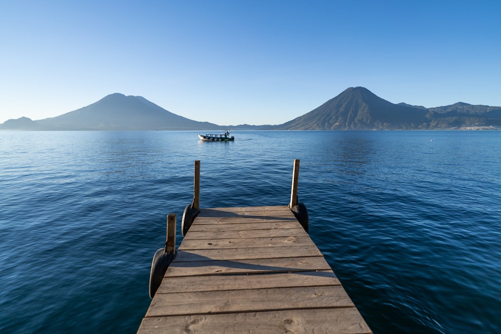 a dock leading out to a boat in the water with Lake Atitlán in the background