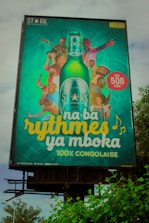 A colorful billboard advertising Stark beer, featuring a large bottle of the beverage in the center surrounded by various people engaging in musical activities. Each individual is shown playing instruments or dancing, with bright and joyful expressions. The text reads 'na ba rythmes ya mboka' and highlights that the product is 100% Congolese.