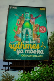 A colorful billboard advertising Stark beer, featuring a large bottle of the beverage in the center surrounded by various people engaging in musical activities. Each individual is shown playing instruments or dancing, with bright and joyful expressions. The text reads 'na ba rythmes ya mboka' and highlights that the product is 100% Congolese.