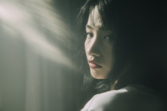 A moody, cinematic portrait of a thoughtful woman in dim lighting with dark feminine tones.
