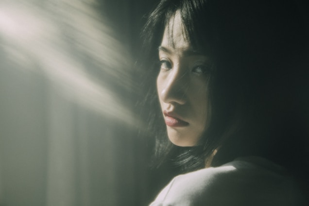 A moody, cinematic portrait of a thoughtful woman in dim lighting with dark feminine tones.