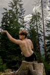 a shirtless man posing on a rock in the woods