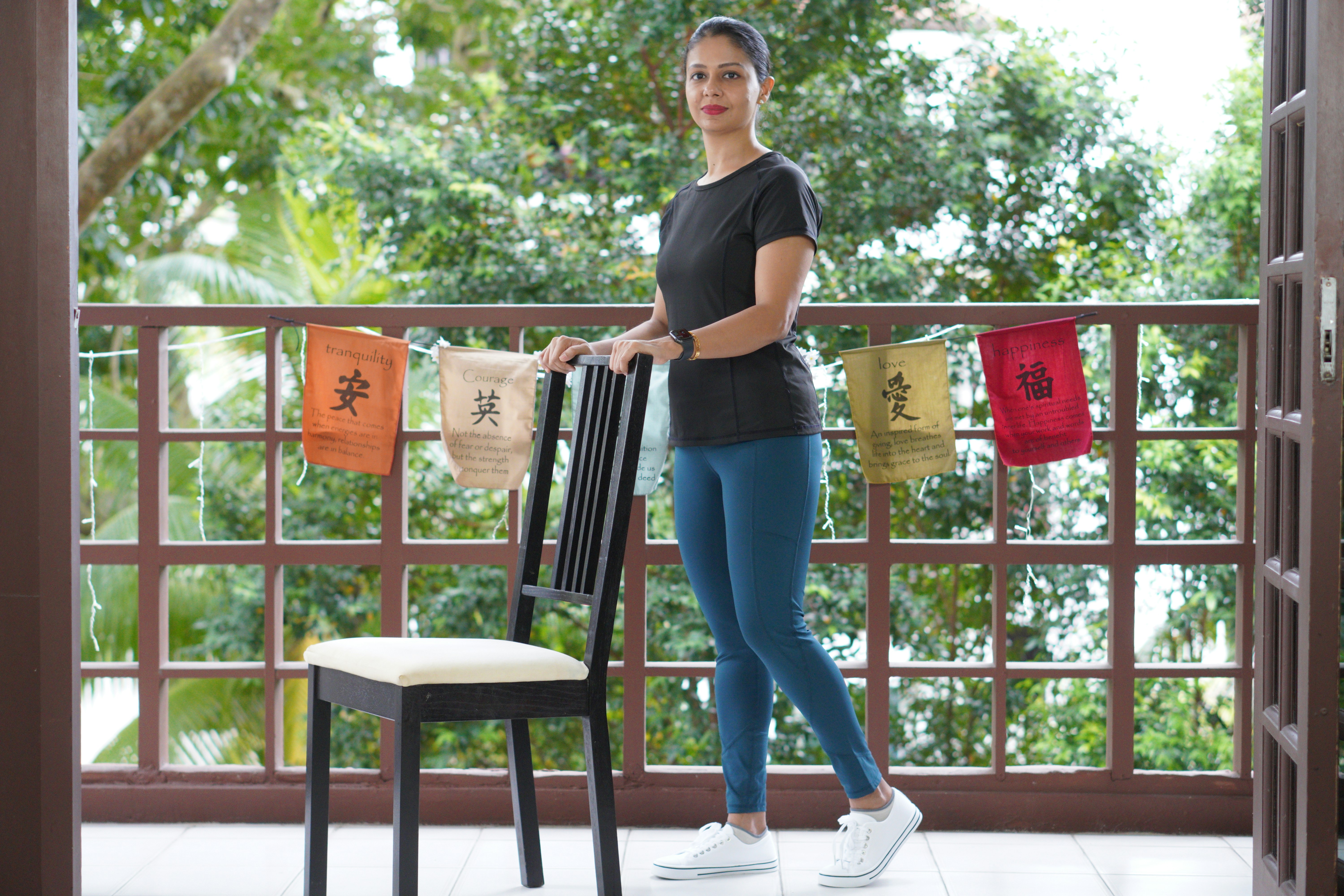 A woman standing beside a wooden chair on a balcony.