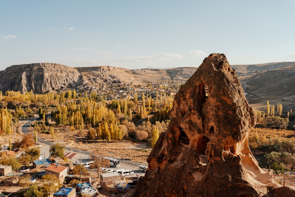 a large rock formation with a town below it with Cappadocia in the background