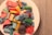 A white plate filled with assorted colorful candies, including various shapes and sizes. The candies are covered in sugar and feature bright colors such as red, yellow, blue, and green. A coiled piece of black candy is also visible.
