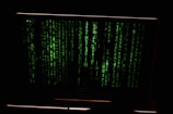 Green digital code streams vertically across the screen, resembling a hacker or cyber interface against a dark background.