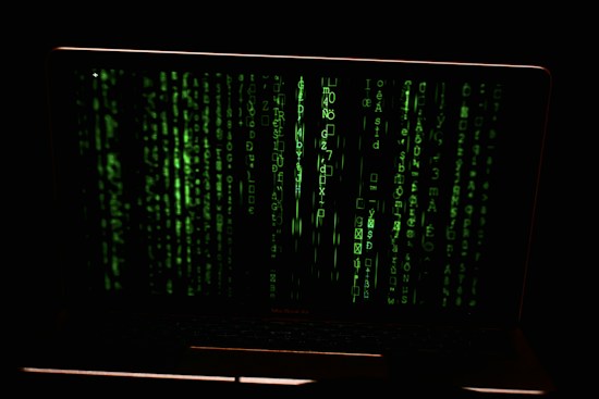 Green digital code streams vertically across the screen, resembling a hacker or cyber interface against a dark background.