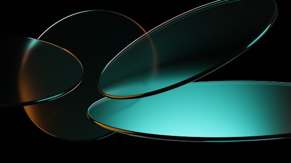 A digital artwork featuring overlapping, elliptical shapes with a glossy finish. The shapes are predominantly turquoise and orange, set against a dark background, creating a sense of depth and fluidity.
