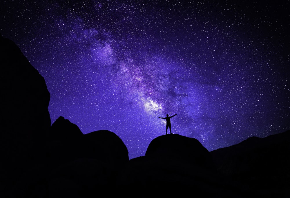 a silhouette of a person standing on a rock with a starry sky above